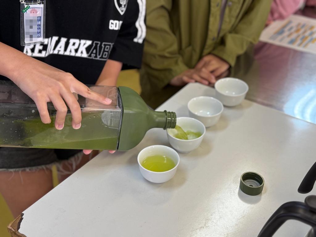 小学生が冷茶ポットからそのぎ茶を注いでいる