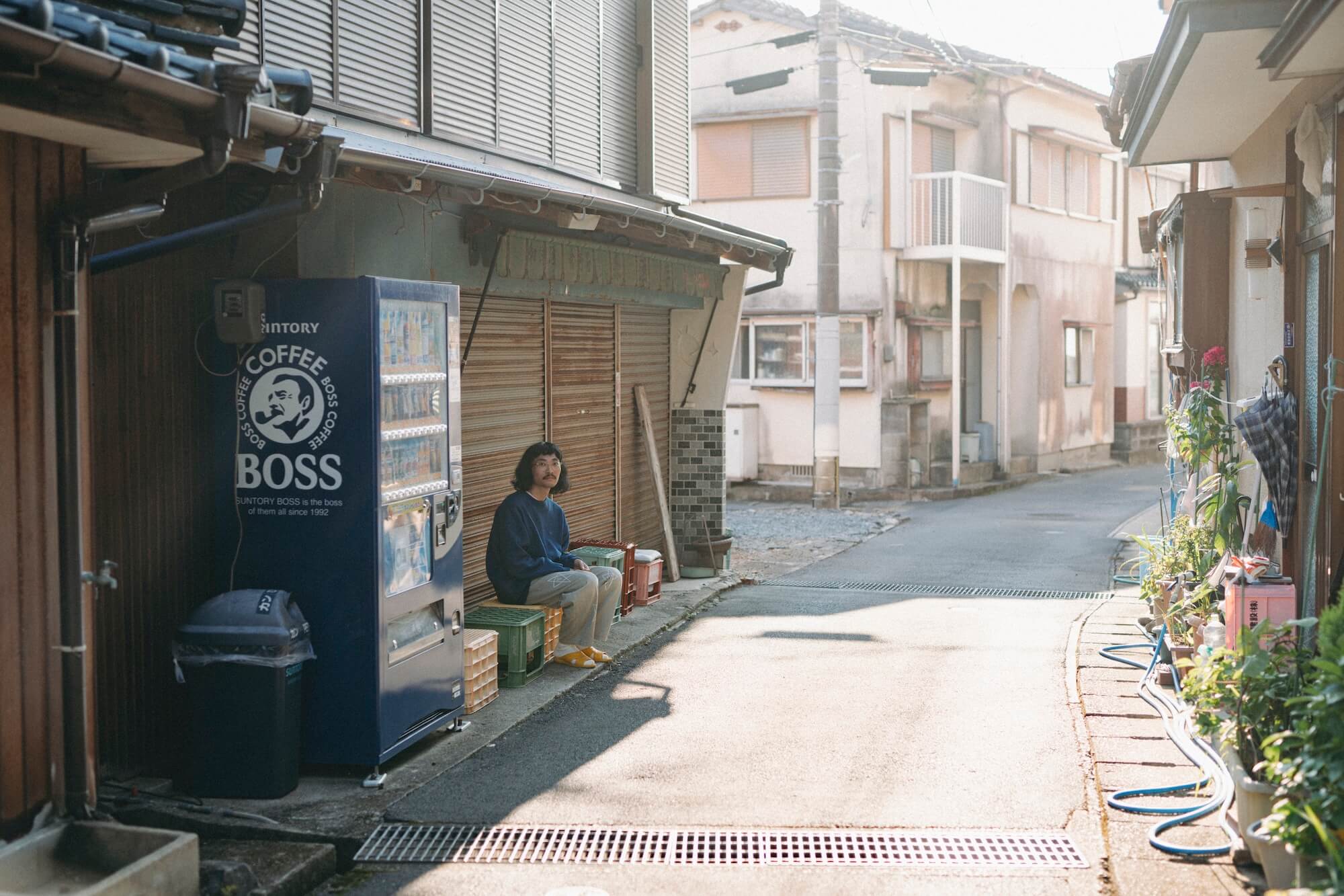 千綿の裏路地に男性が一人座ってこちらを見ている