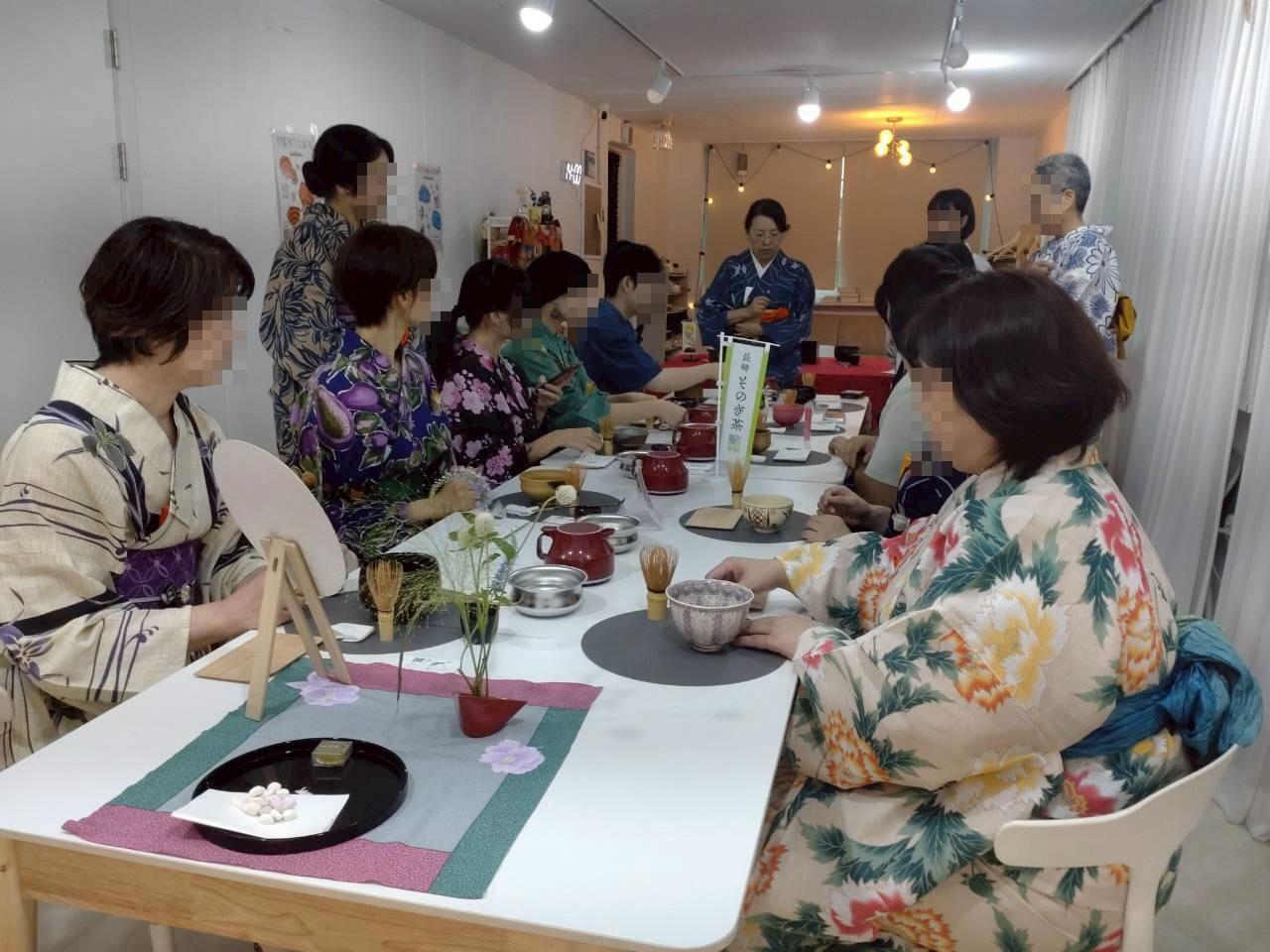 テーブルを囲んだ多国籍の浴衣姿の人々がそのぎ抹茶を楽しんでいる