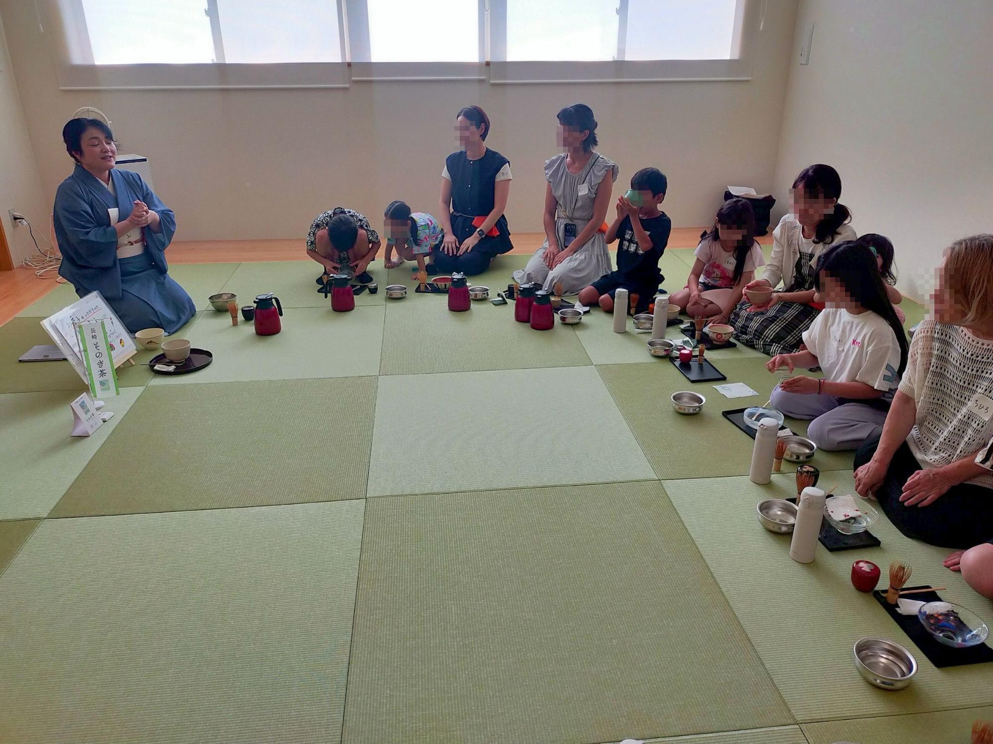 畳の上のお盆に茶器セットが置かれ親子で抹茶を楽しんでいる