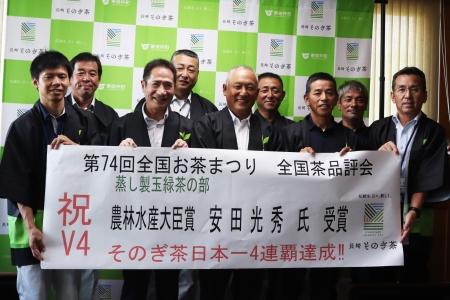 男性たちが受賞を祝う横断幕を持って笑顔で写っている写真