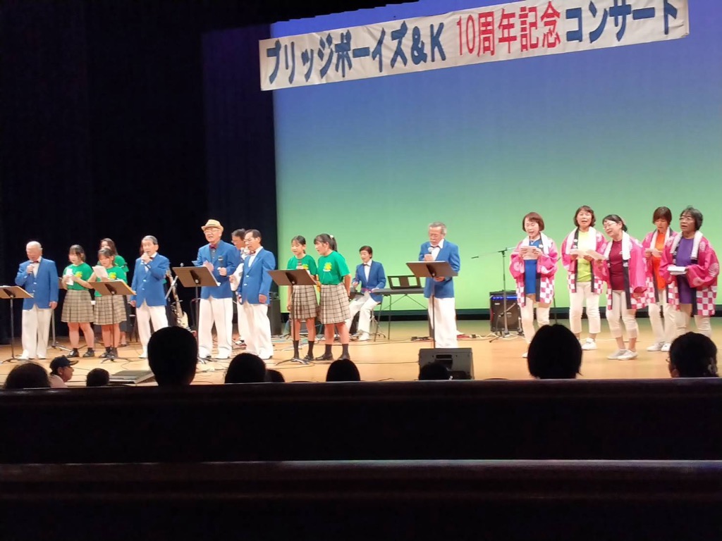 ステージの上に多世代の人が並んで歌を歌っている