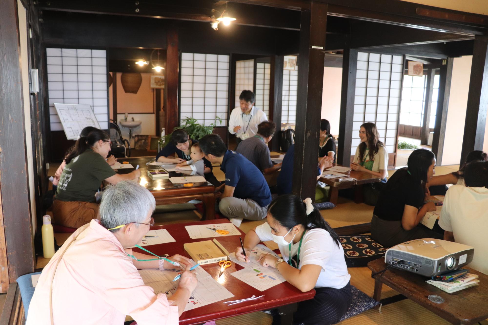 明治の民家に15名ほどの人が集まって座っている