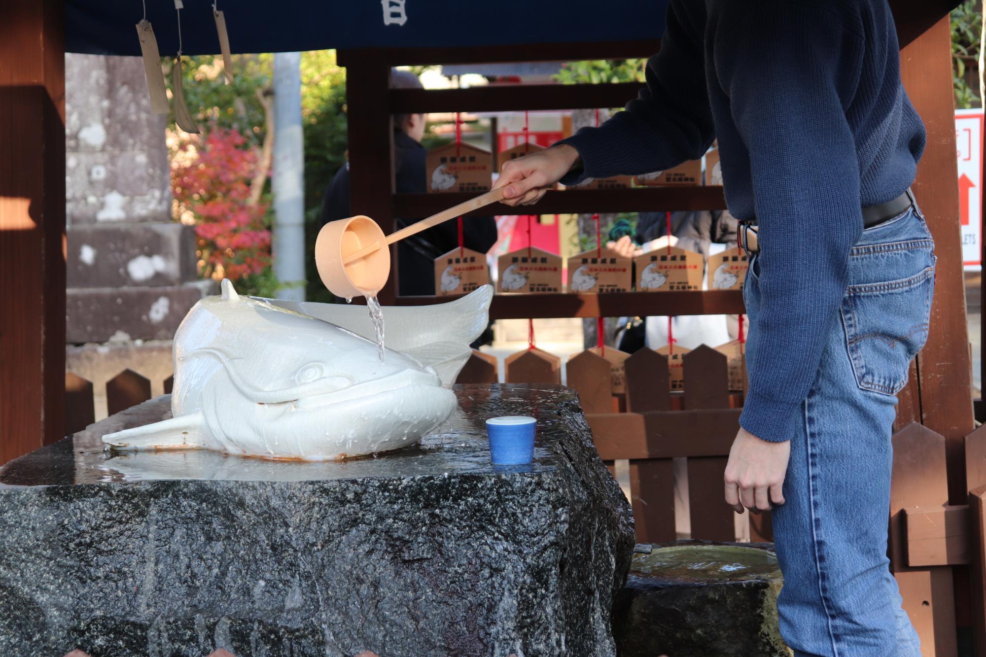 白いなまずのオブジェにひしゃくで水をかけている