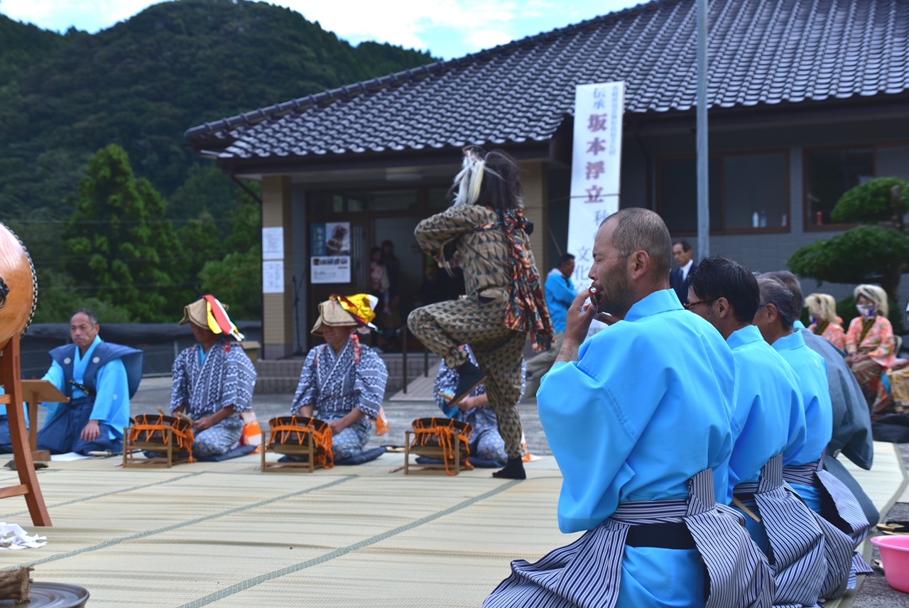 屋外で太鼓と笛を男性たちが奏で中央で鬼が踊っている